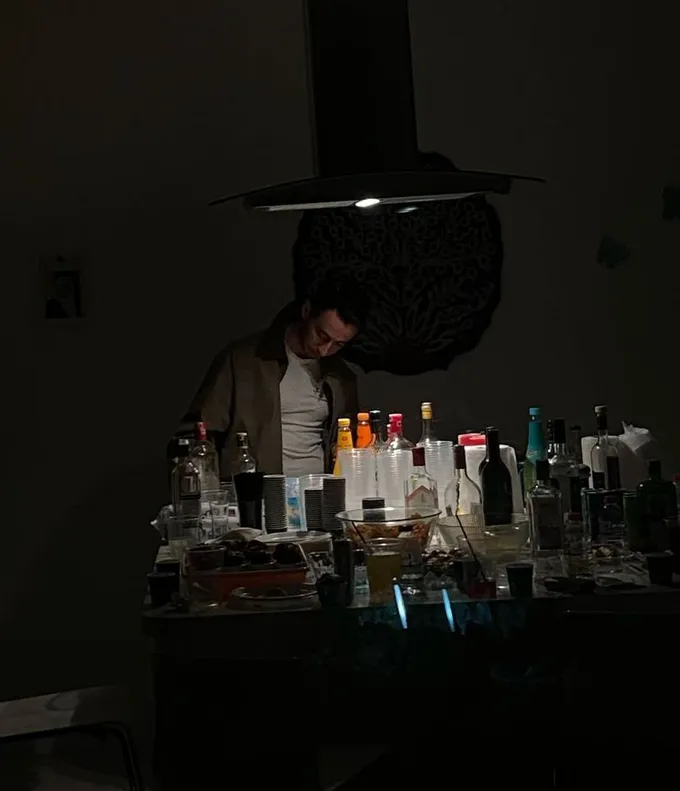 Ömer Batuhan Tandoğan hosting friends at a house party, standing behind a table full of drinks