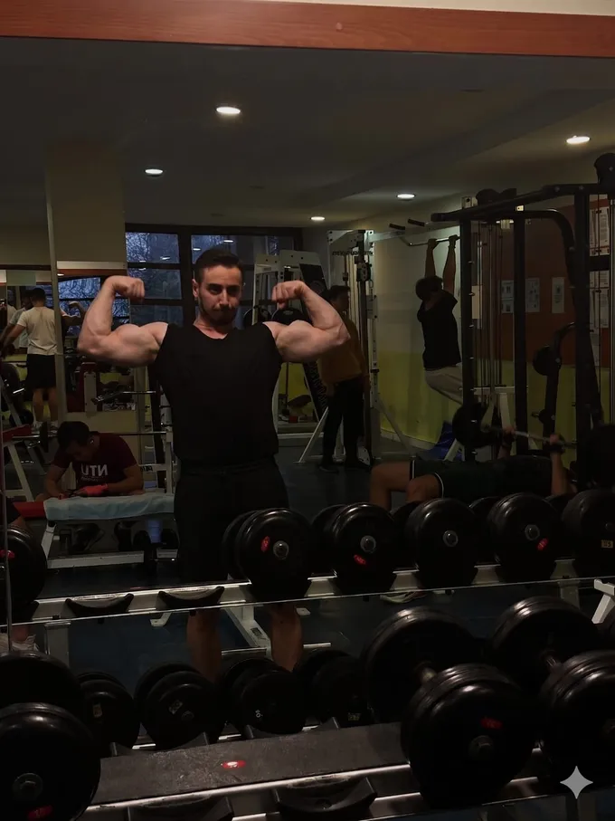 Ömer Batuhan Tandoğan flexing his biceps in front of a gym mirror during a bodybuilding workout